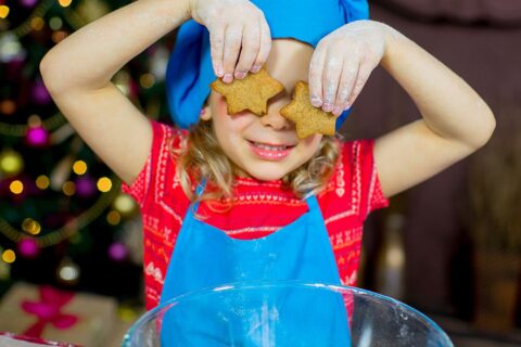 Adorable young girl with a radiant smile playfully concealing her eyes using star-shaped cookies