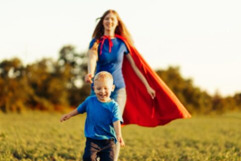 Joyful young boy running through an open field while his mother chases after him