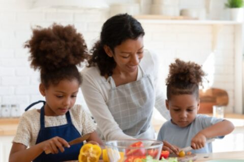 Mother teaching her two young daughters how to cut peppers