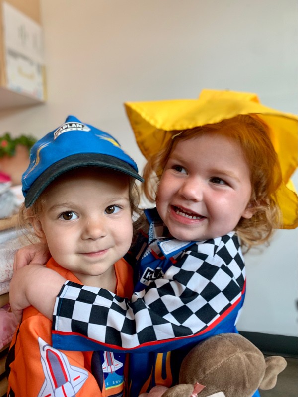 Happy toddler friends dressed in costumes sharing a hug at Lionheart Children's Academy