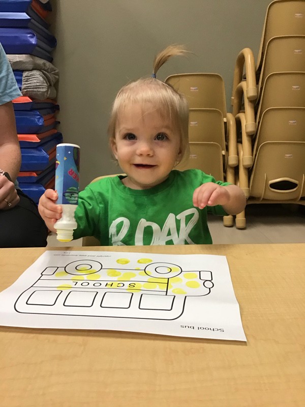 Joyful little girl decorating school bus drawing with yellow stamps at Lionheart Children's Academy
