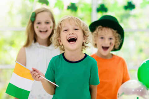 Kids wearing green in front of a shamrock garland and carrying an Irish flag in celebration of St. Patrick's Day.